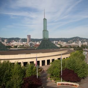 The Oregon Convention Center\'s twin green glass spires rise into a blue sky while downtown sparkles in the background.
