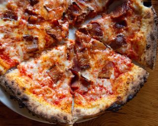 a pizza topped with red sauce, cheese and meat atop a wooden table