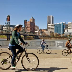 bikers riding along the east bank of the Willamette river with the Hawthorne bridge and Portland downtown buildings in background