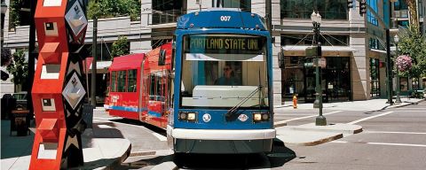 A streetcar passes by a large, red sculpture in front of a building with a neon sign reading, \"Go By Streetcar\"