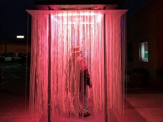 a person walks through a light installation containing long strands of lights hanging from a panel overhead