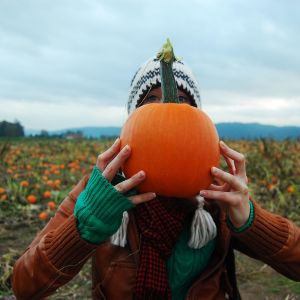 a person standing in front of a pumpkin patch holding a pumpkin in front of their face