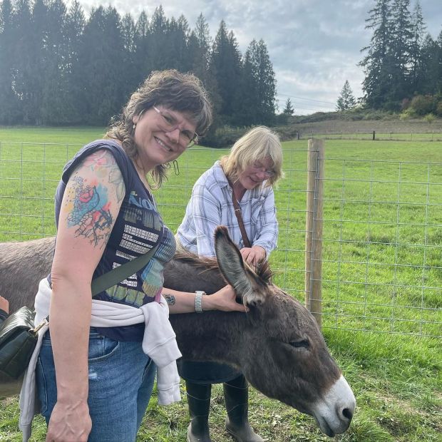 two women petting a donkey in a pasture