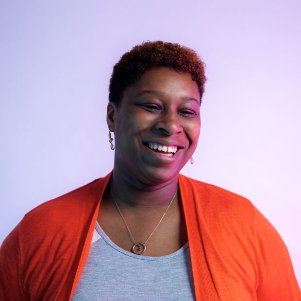 a headshot of a smiling person in an orange cardigan