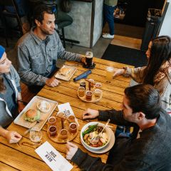 a group of four around a wooden table enjoy draft beers and pub food