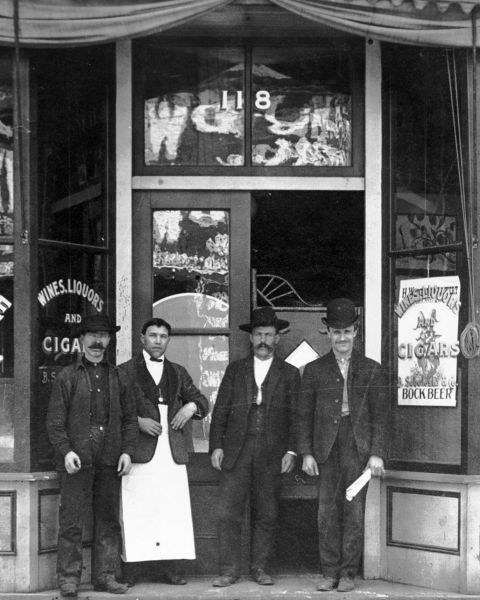 a black and white photo of three men standing in front of a saloon