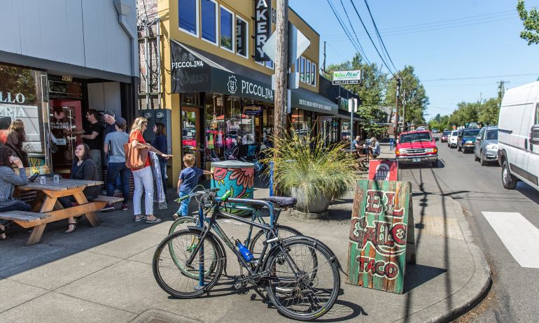 People dining at an outdoor table on the sidewalk while others walk by in the Woodstock neighborhood