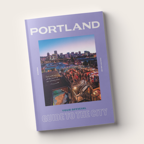 a copy of the Travel Portland Visitor Guide which features an image of Portland surrounded by a purple frame and the words \"Portland your official guide to the city\"